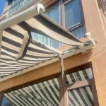 Retractable awning with torn fabric and damaged folding arms after strong wind