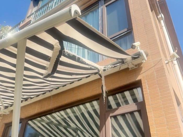 Retractable awning with torn fabric and damaged folding arms after strong wind